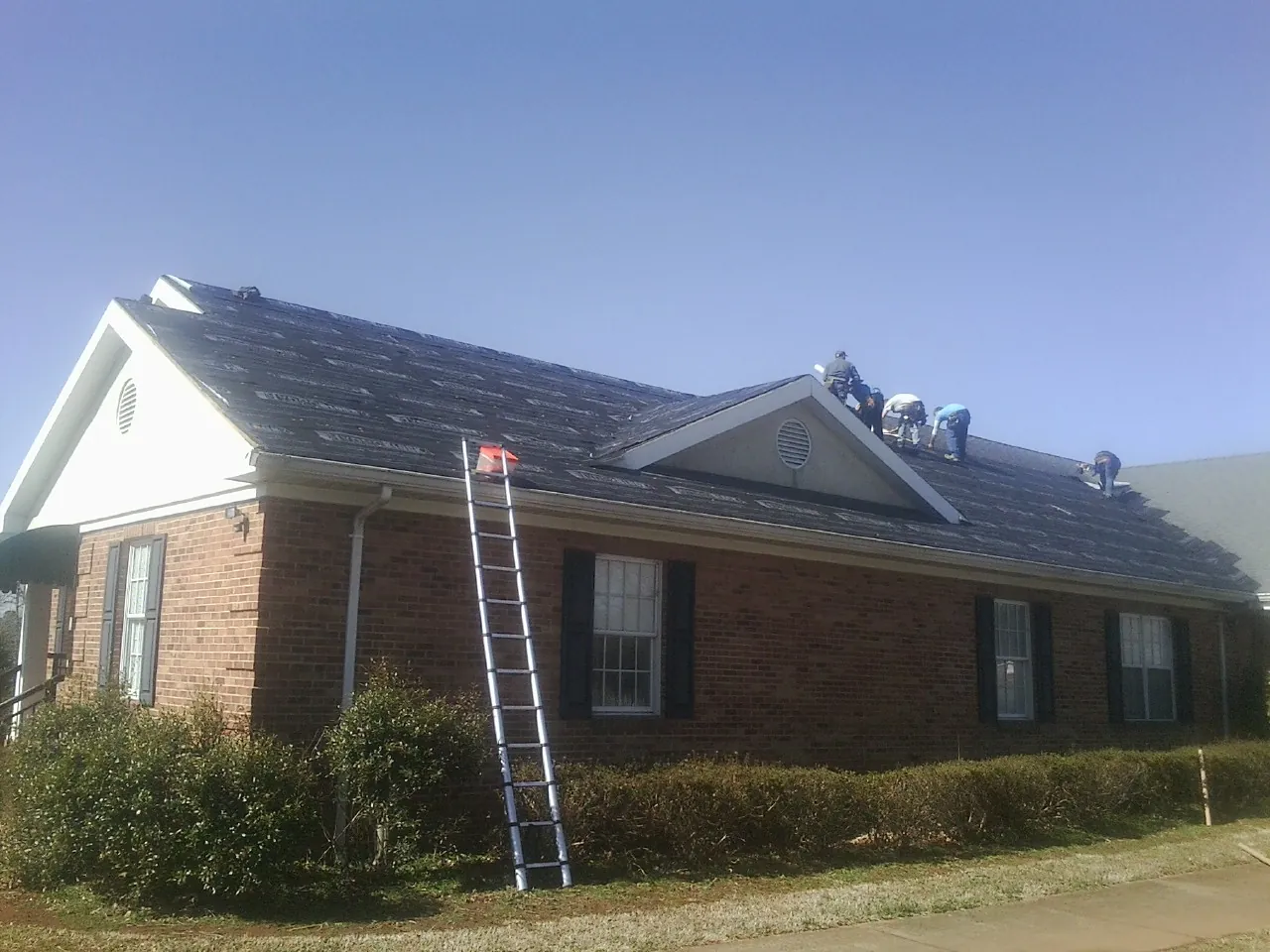 Crew tearing shingles off a brick ranch roof with a ladder set — Metal Roof Repair work by our crew in Midland