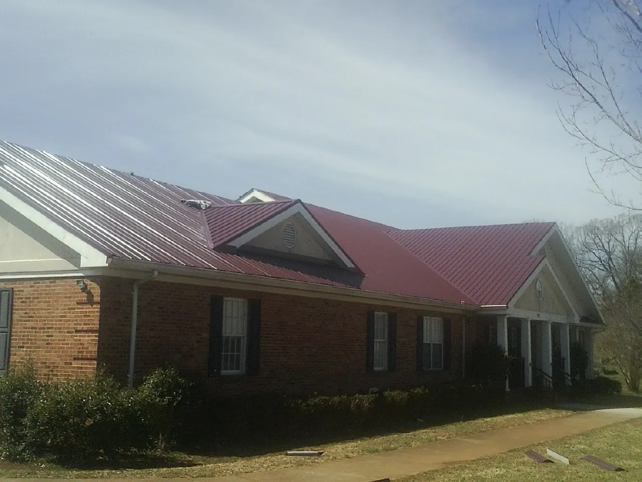 Red metal roof with gabled entries on a long brick building, from a Hail Damage Roof Repair job in Midland